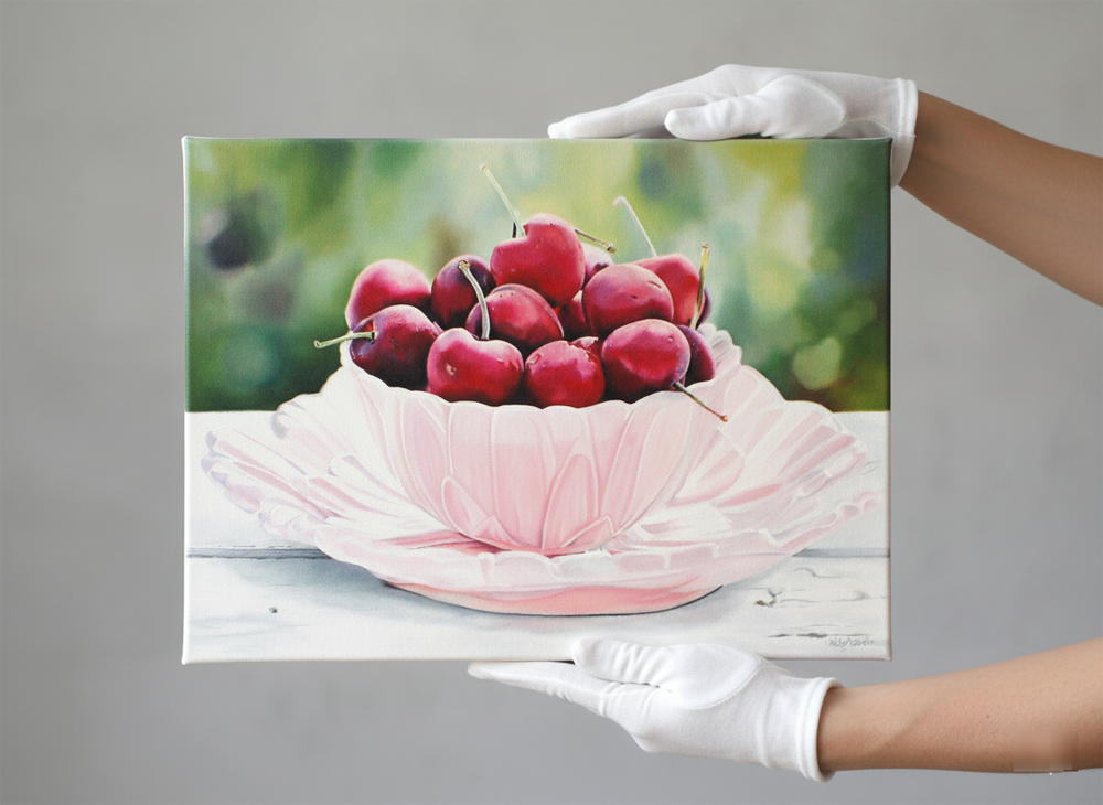 A close-up shot captures a vibrant still life painting featuring a bowl of ripe red cherries, held by white-gloved hands against a neutral background. The painting, presented on a gallery wrap canvas, measures 70x50cm with a 2cm depth, showcasing rich colors and intricate details that highlight the succulent fruit and delicate bowl.