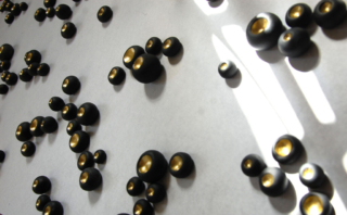black clay wall pods with metallic gold centers, abstract wall installation of 300 pods for interior desig project.