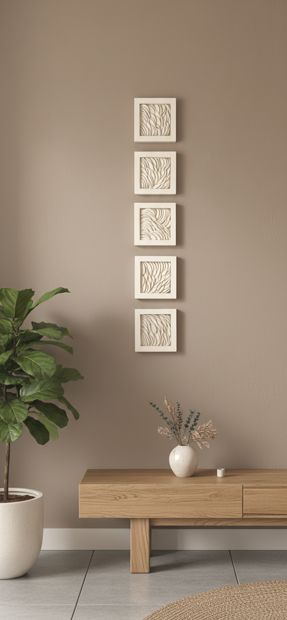 Five square, white-framed clay dimensional artworks, each 10x10 cm, are arranged vertically on a warm taupe wall in a modern organic aesthetic room. To the left, a large fiddle leaf fig tree in a white pot adds a touch of greenery. Below the artworks, a minimalist wooden console table holds a white vase with dried botanicals and a small white object, possibly a candle or diffuser. The floor is covered with light gray tiles, and a circular braided rug in a natural fiber peeks into the frame from the bottom right. The overall impression is one of serene, understated elegance.