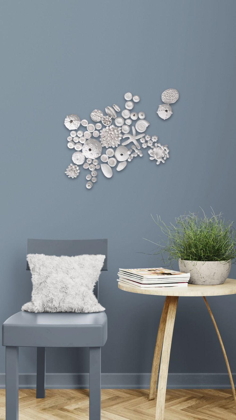 A collection of approximately 60 white, handcrafted clay marine life elements—including various coral forms, sea urchin shells, a starfish, and abstract shell shapes—artfully clustered on a pale blue textured surface, designed for a DIY wall art installation.