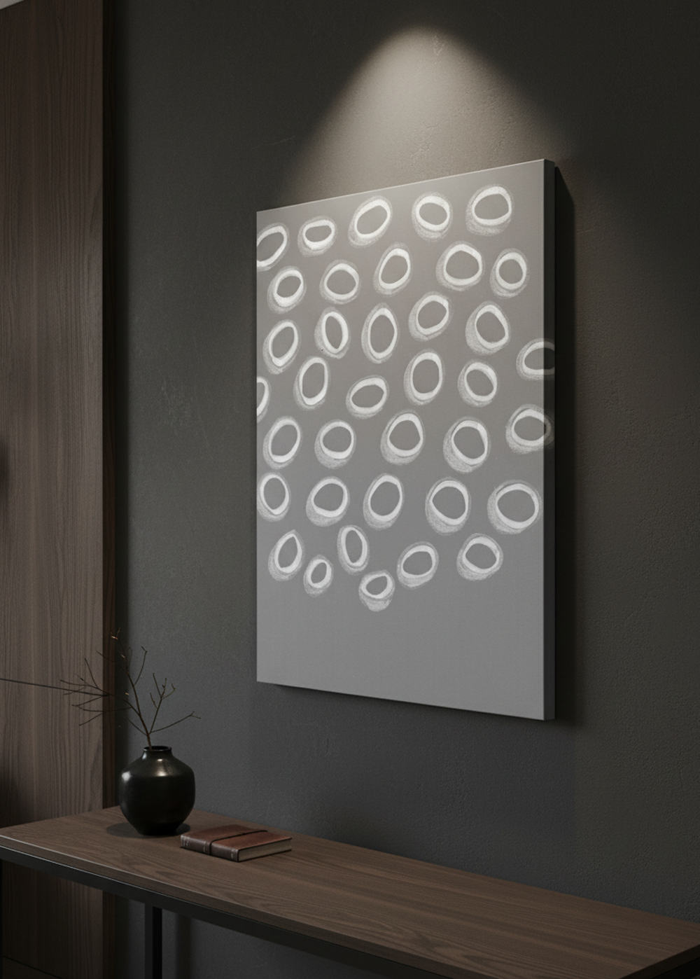 A gallery-wrapped canvas painting, sized 70 x 50 cm, depicting white abstract oval shapes on a gray background, is showcased in a modern dark luxury interior. The canvas is hung on a dark wall, with a partial view of a luxurious room featuring dark furniture and minimalist decor. The shot is a sideways close-up, emphasizing the texture of the canvas and the elegant simplicity of the artwork within its sophisticated setting.