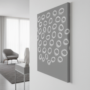 A close-up, sideways shot shows a 70 x 50 cm gallery-wrapped canvas hanging on a white wall in a luxurious, white and gray interior. The canvas features a painting of various white, hand-drawn oval shapes on a gray background, suggesting an abstract and organic pattern. In the softly blurred background, a contemporary gray armchair, a light-colored sculptural vase on a minimalist side table, and a large window with sheer white curtains are visible, enhancing the sophisticated and elegant atmosphere of the space.